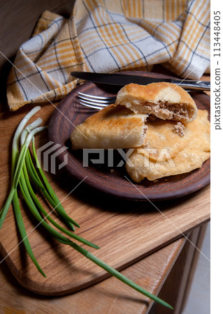 Clay plate of fried meat pies with cutlery and green onion on wooden table. Clay plate of fried meat pies with cutlery and green onion on wooden table. 113448405
