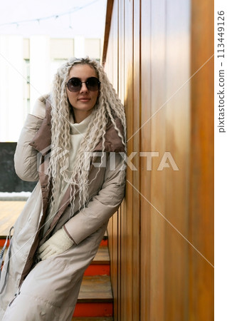 Woman Leaning Against Wall in Coat and Sunglasses Woman Leaning Against Wall in Coat and Sunglasses 113449126