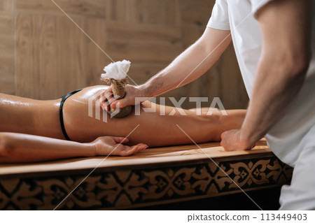 Side view of Herbal Ayurvedic massage with Kizhi Herbal Bags on buttocks. Relaxed female client receiving herbal bolus bags massage. Tranquil and serenity of aromatherapy recreation at spa salon. 113449403
