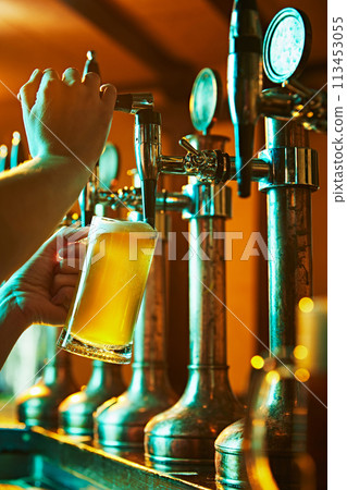 Male hands, bartender pouring delicious crafted beer from taps in glass. Warm atmosphere of bar, pub. Refreshment and relaxation 113453055