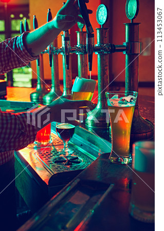 Beer culture. Bartender's hands pouring lager foamy beer from the taps with precision and care in mugs 113453067