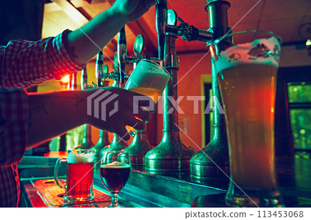 Male hand, bartender pouring foamy lager beer from tap into glass. Bar,, pub worker serving beer mug to customer 113453068