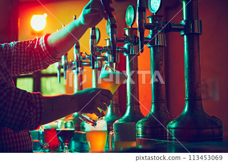 Male hand, bartender pouring foamy lager beer from tap into glass. Bar,, pub worker serving beer mug to customer 113453069
