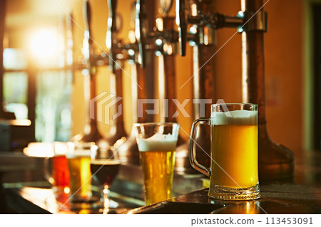 Glasses with various foamy beer tastes on wooden counter standing near beer taps. Modern bar, pub aesthetics Glasses with various foamy beer tastes on wooden counter standing near beer taps. Modern bar, pub aesthetics 113453091