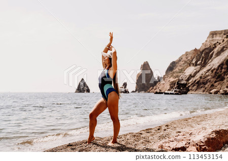 Woman beach vacation photo. A happy tourist in a blue bikini enjoying the scenic view of the sea and volcanic mountains while taking pictures to capture the memories of her travel adventure. 113453154