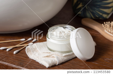 Opened cosmetic cream jar on folded towel near basin on wooden counterto in bath, lid mockup Opened cosmetic cream jar on folded towel near basin on wooden counterto in bath, lid mockup 113453580