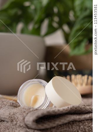 Opened lip balm jar on folded towels near basin and green monstera in bath, lid mockup Opened lip balm jar on folded towels near basin and green monstera in bath, lid mockup 113453581