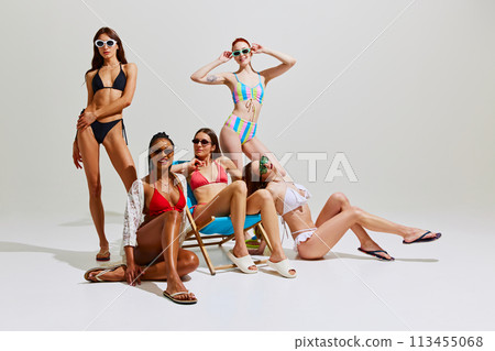 Elegance and refinement. Beautiful, slim girl in swimsuits and sunglasses posing against white studio background. 113455068