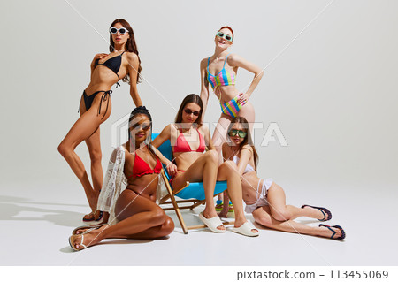 Essence of summer mood. Young slim girls in swimsuits and sunglasses look fresh and vibrant against white studio background. 113455069