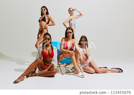 Beautiful girls in swimsuits and sunglasses create striking image of summer relaxation and rejuvenation against white studio background. 113455070