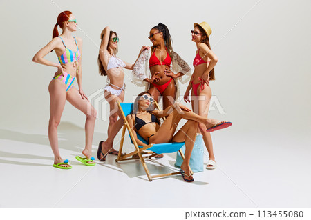 Beautiful young girls, friends in swimsuits and sunglasses look stylish and elegant against white studio background. Beautiful young girls, friends in swimsuits and sunglasses look stylish and elegant against white studio background. 113455080