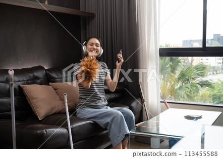 Cheerful young woman having fun cleaning house, singing and using duster as microphone Cheerful young woman having fun cleaning house, singing and using duster as microphone 113455588