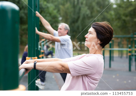 Elderly woman doing exercises in sports bars on outdoor sports ground Elderly woman doing exercises in sports bars on outdoor sports ground 113455753
