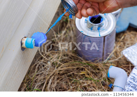 Plumber sealing a pvc plastic pipe with glue before gluing it 113456344