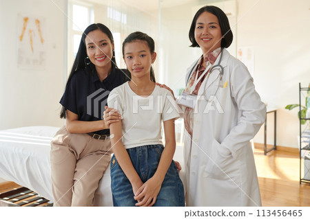 Smiling pediatrician standing next to teenage patient and her mother 113456465