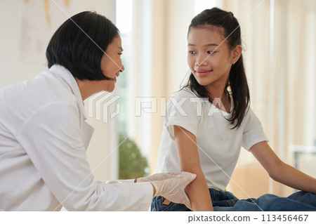 Cheerful doctor sticking patch on injured elbow on teenage girl 113456467