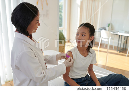 Smiling doctor sticking bandage on injection site on arm of teenage girl 113456468