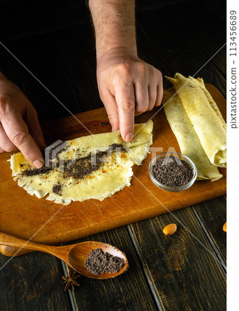 The cook rolls pancakes with his hands on the kitchen board. Low key concept of preparing dessert in the kitchen The cook rolls pancakes with his hands on the kitchen board. Low key concept of preparing dessert in the kitchen 113456689
