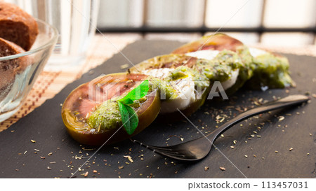 Caprese salad with mozzarella, black tomatoes and pesto on black stone plate 113457031