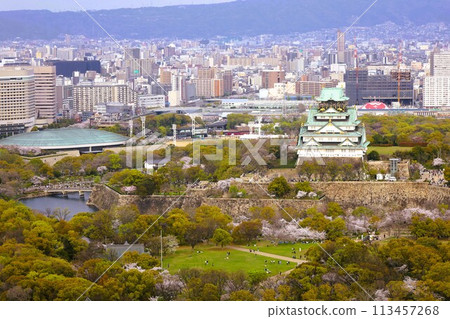 Bird's-eye view of Osaka Castle from the sky Cherry blossom season Ikoma mountain range Cherry blossoms in full bloom against the blue spring sky 113457268