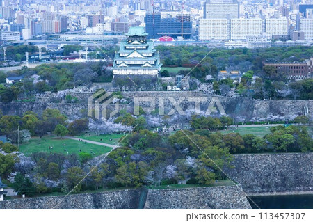 Bird's-eye view of Osaka Castle from the sky Cherry blossom season Ikoma mountain range Cherry blossoms in full bloom against the blue spring sky 113457307