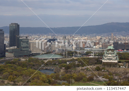 Bird's-eye view of Osaka Castle from the sky Cherry blossom season Ikoma mountain range Cherry blossoms in full bloom against the blue spring sky 113457447