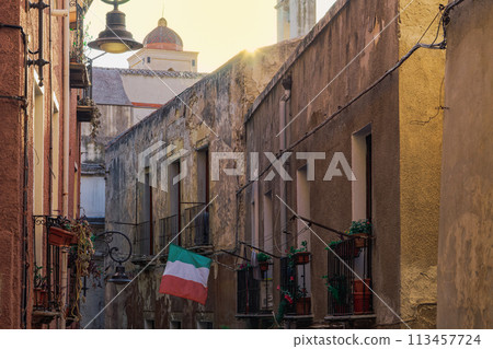 Cagliari citadel alley with traditional buildings with iron balconies and Italian flag waving in Sardinia Island, Italy. 113457724