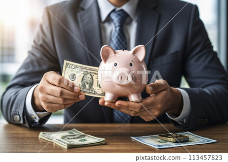 A business man holds dollar bills and a piggy bank in his hand A business man holds dollar bills and a piggy bank in his hand 113457823