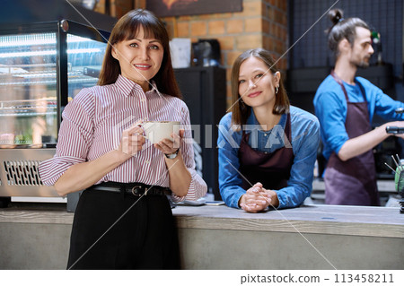 Woman customer of coffee shop near counter with cup of coffee Woman customer of coffee shop near counter with cup of coffee 113458211