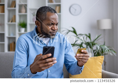 African American man experiences confusion and potential fraud while using his credit card and smartphone in a well-lit room. African American man experiences confusion and potential fraud while using his credit card and smartphone in a well-lit room. 113458326