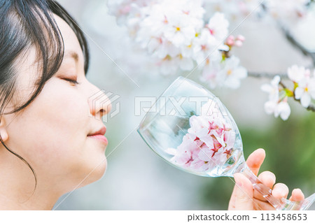 Woman holding a wine glass filled with cherry blossom petals 113458653