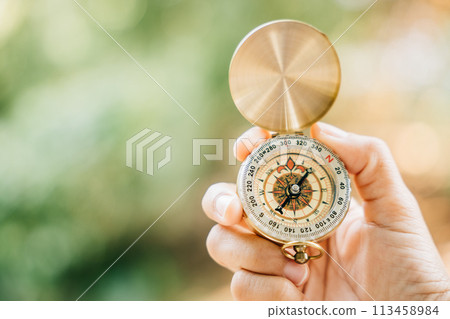 With a picturesque forest and tranquil lake in the background a woman's hand securely holds a compass symbolizing guidance and the exciting exploration that awaits. 113458984