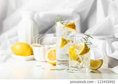 Summer refreshing lemonade drink or alcoholic cocktail with ice, rosemary and lemon slices on the white table. 113458992