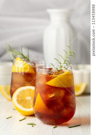 Iced tea or alcoholic cocktail with ice, rosemary and lemon slices on the white table. 113458998