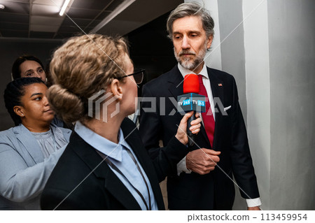 American politician walks in corridor of government building, answers press questions 113459954