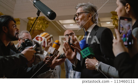 Mature diplomat surrounded by crowd of journalists 113460111