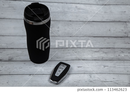 A car key with automatic buttons and a thermocup are black with metal inserts on a white wood background with a place for text. High quality photo 113462623