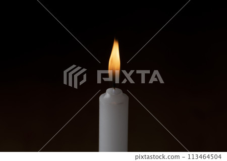 A lit candle on a dark background 113464504
