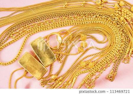 Many gold necklaces and gold bars on pink velvet cloth. 113469721