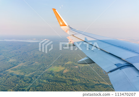 View of airplane wing, blue skies and green land during landing. Airplane window view. 113470207
