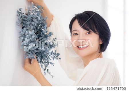 A middle-aged woman smiling while holding a eucalyptus wreath A middle-aged woman smiling while holding a eucalyptus wreath 113471700
