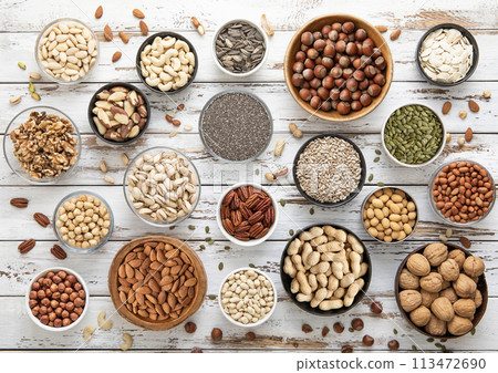 Mixed assorted raw healthy nuts and seeds in various bowls on light wooden table. 113472690