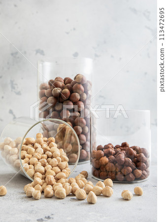 Glass jars with healthy raw hazelnut whole and peeled nuts on white kitchen table. 113472695