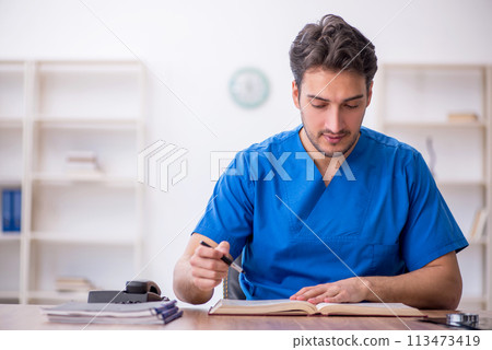 Young male doctor student reading book in the clinic Young male doctor student reading book in the clinic 113473419