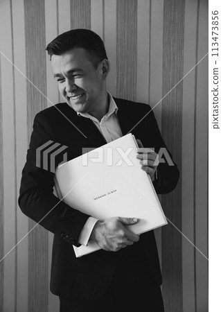 A man holds a photo book in a white leather cover A man holds a photo book in a white leather cover 113473856