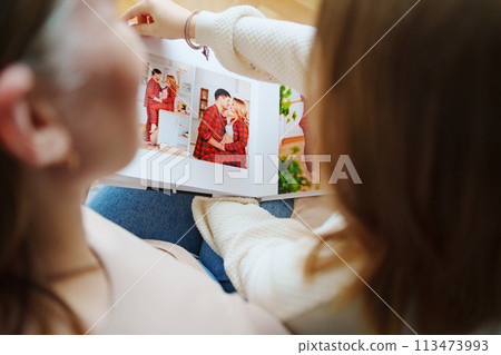 mother and daughter flips through a book with photos of dad and pregnant mom. mother and daughter flips through a book with photos of dad and pregnant mom. 113473993