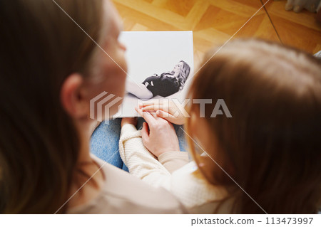 mother and daughter flips through a book with photos of dad and pregnant mom. mother and daughter flips through a book with photos of dad and pregnant mom. 113473997