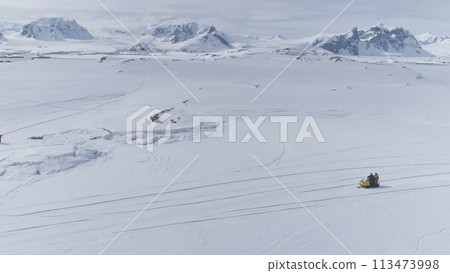 Aerial Flight Over Fast Moving Snowmobile Ski-Doo. Antarctica Landscape. Man Riding On Vintage On Snow Covered Land. Polar Ocean, Mountains Background. Extreme Outdoor Activity. Aerial Flight Over Fast Moving Snowmobile Ski-Doo. Antarctica Landscape. Man Riding On Vintage On Snow Covered Land. Polar Ocean, Mountains Background. Extreme Outdoor Activity. 113473998