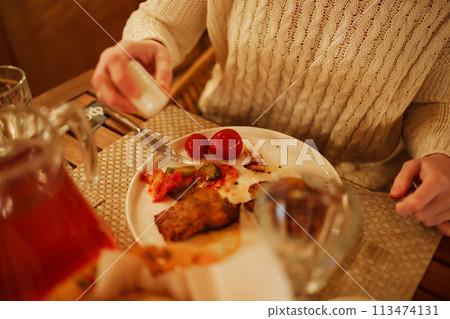a plate of fish, potatoes and pickled vegetables and hands with a knife and fork 113474131