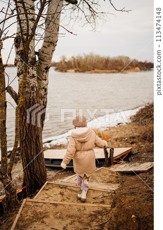 Teenage girl in winter clothes going down the stairs on the ice on the bank.  113474148
